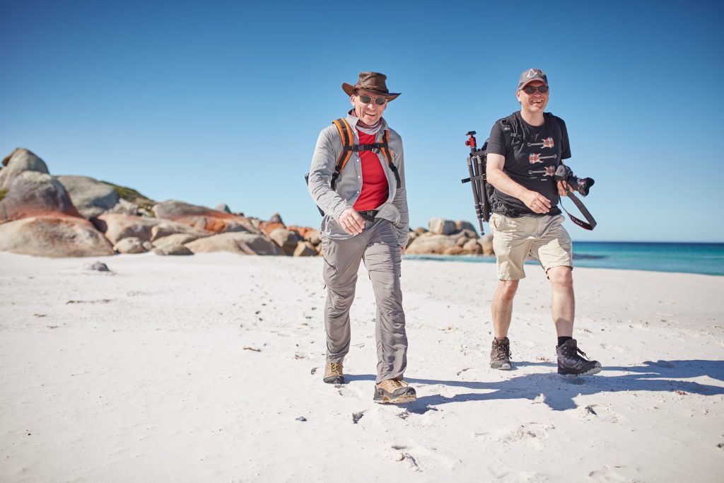 Tour guide and guest walking on a beach in the Bay of Fires, Tasmania in a conservation area.